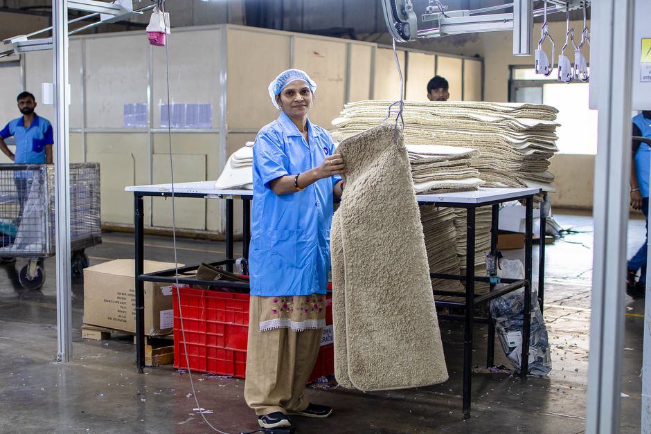 A textile worker processes rugs in a busy factory environment, showcasing industry and manual labor.